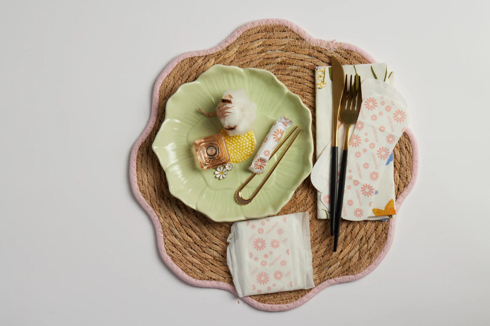 Green plate with cotton and Femieko products on a mat with a pink edge